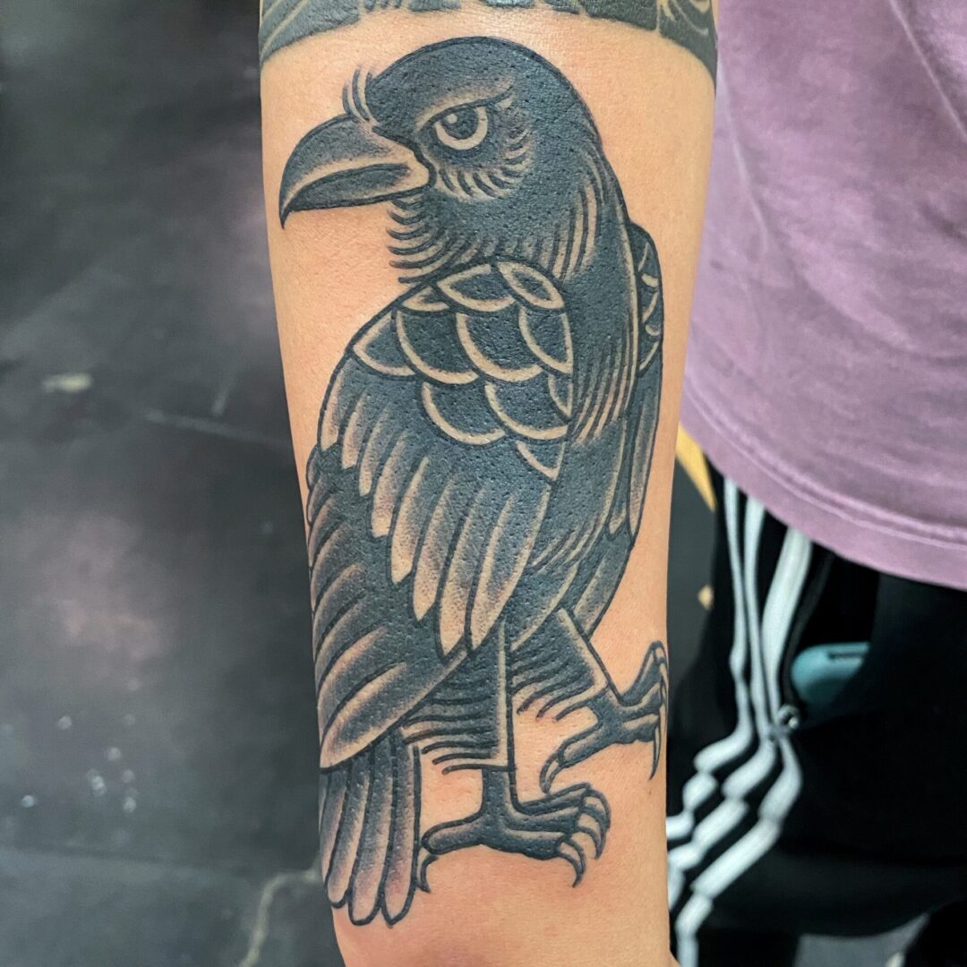 A black and grey tattoo of a bird on the arm.