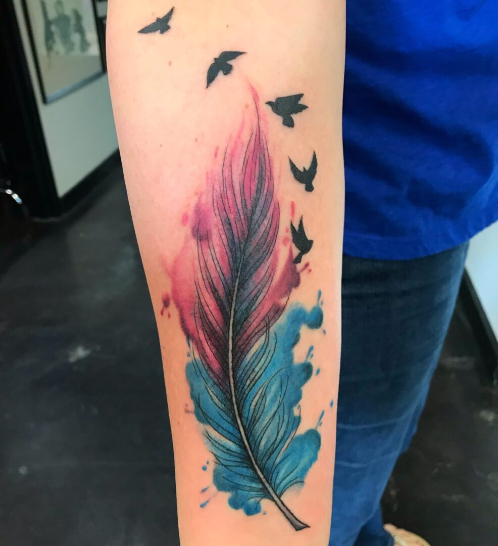 A tattoo of a feather and birds flying around it.