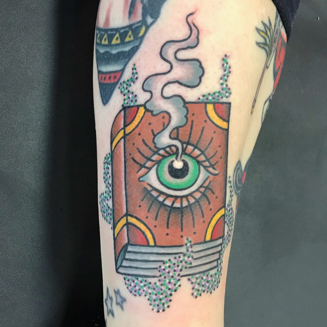 A tattoo of an eye and book on the arm.
