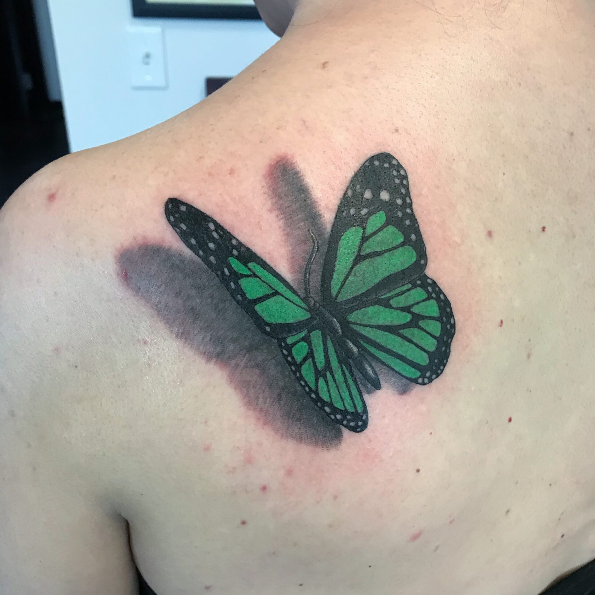 A green butterfly tattoo on the back of someone 's shoulder.