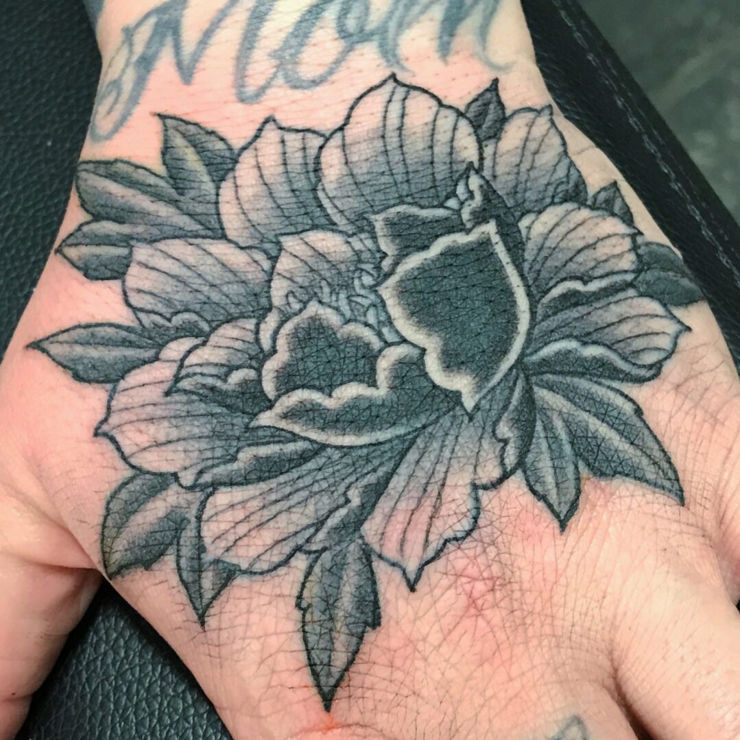A black and white tattoo of a flower on the hand.