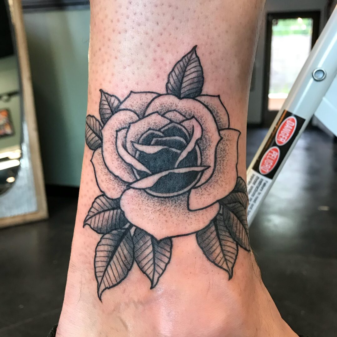 A black and white rose tattoo on the ankle of a person.