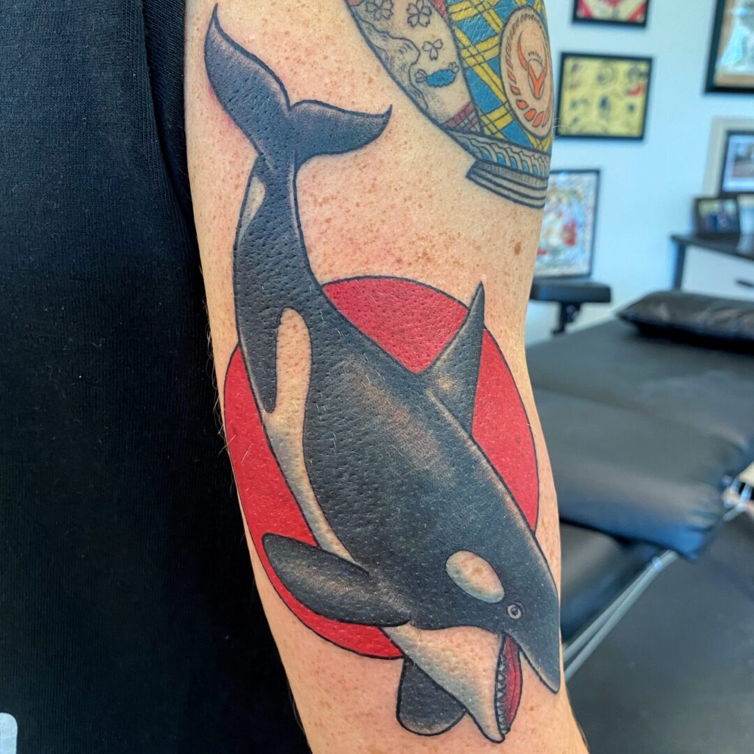 A tattoo of an orca whale with a red circle around it.
