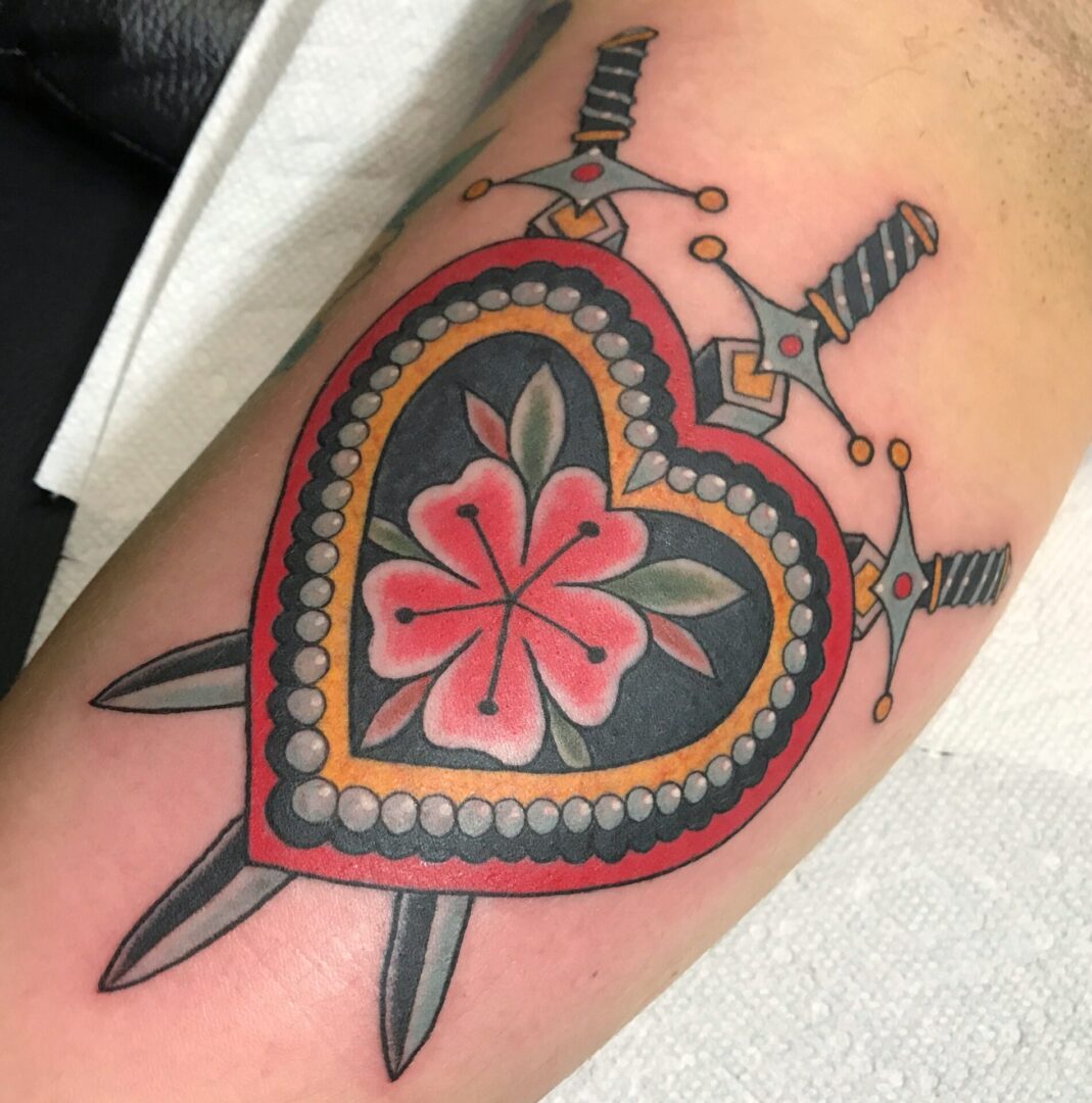A tattoo of a heart with flowers and two swords.