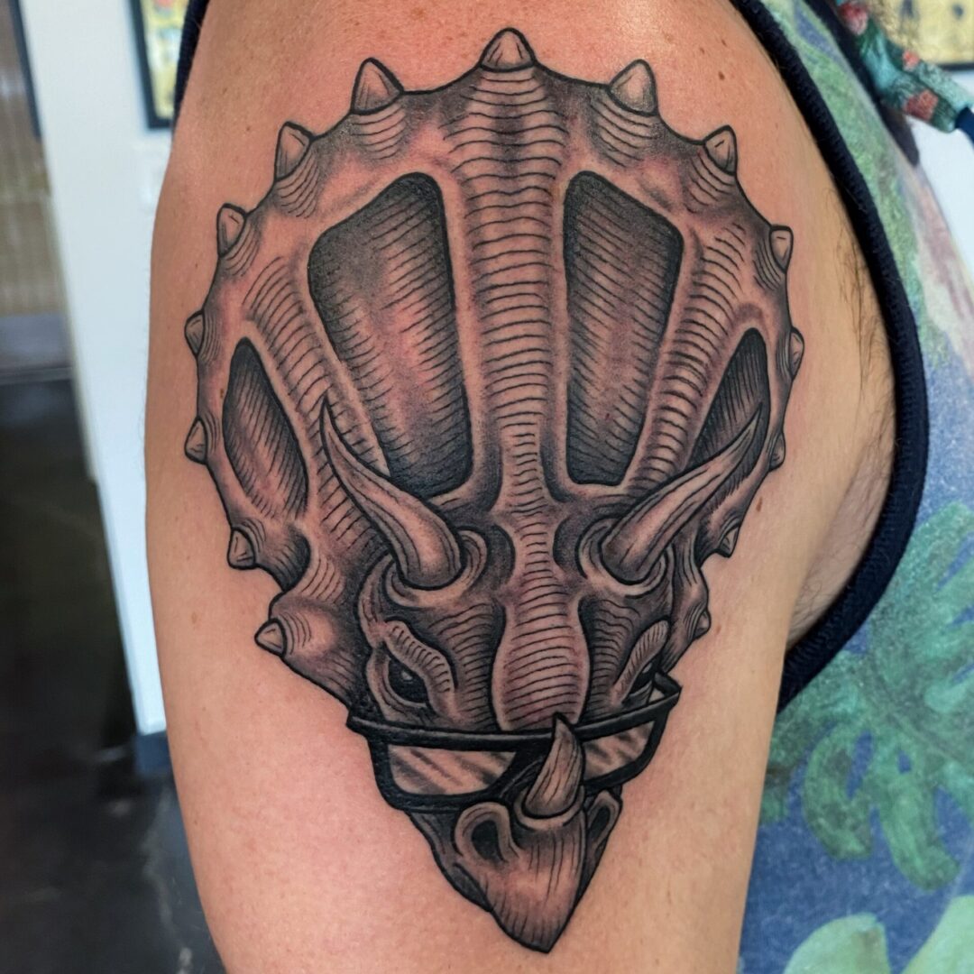 A black and white tattoo of a triceratops