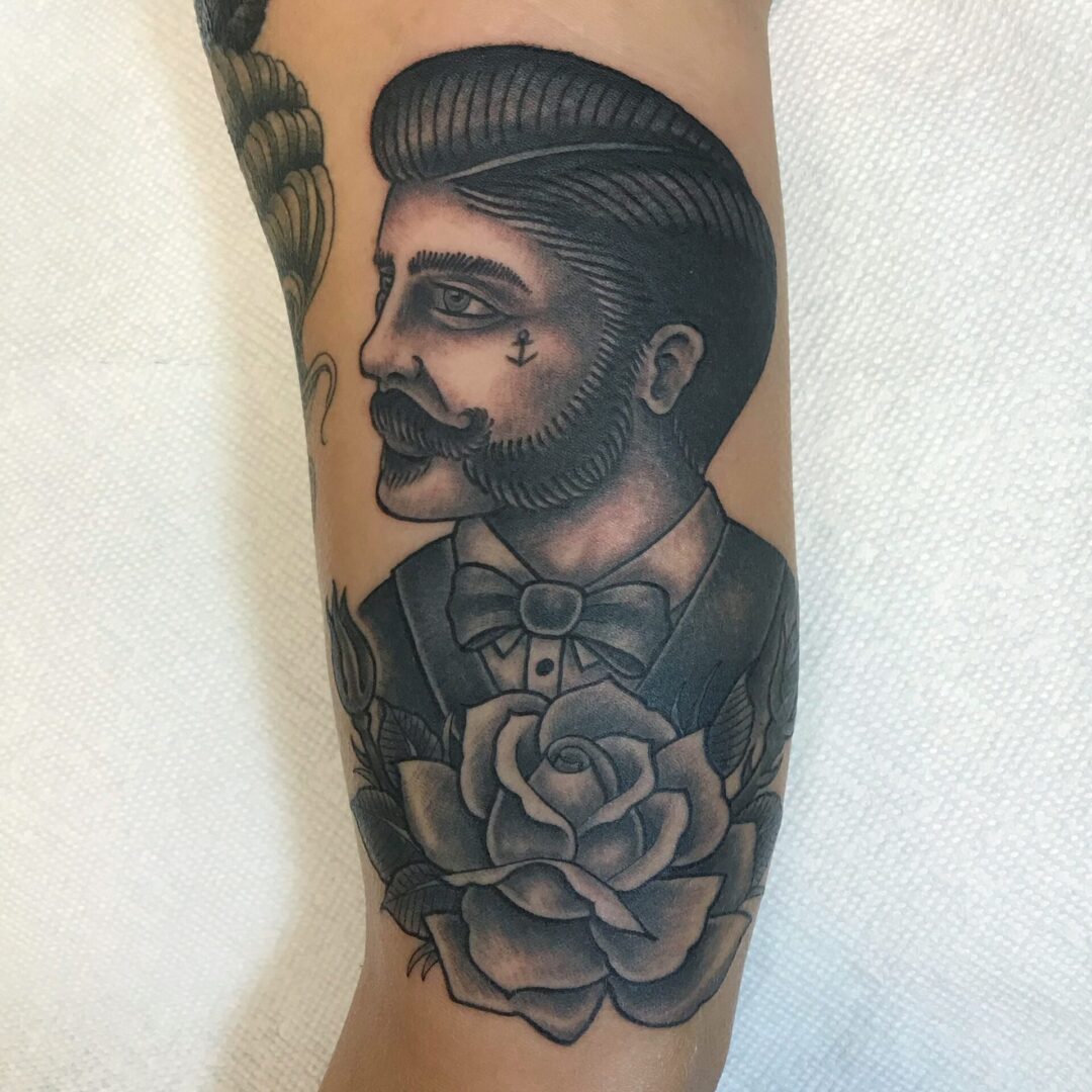 A man with a beard and mustache is tattooed on his arm.