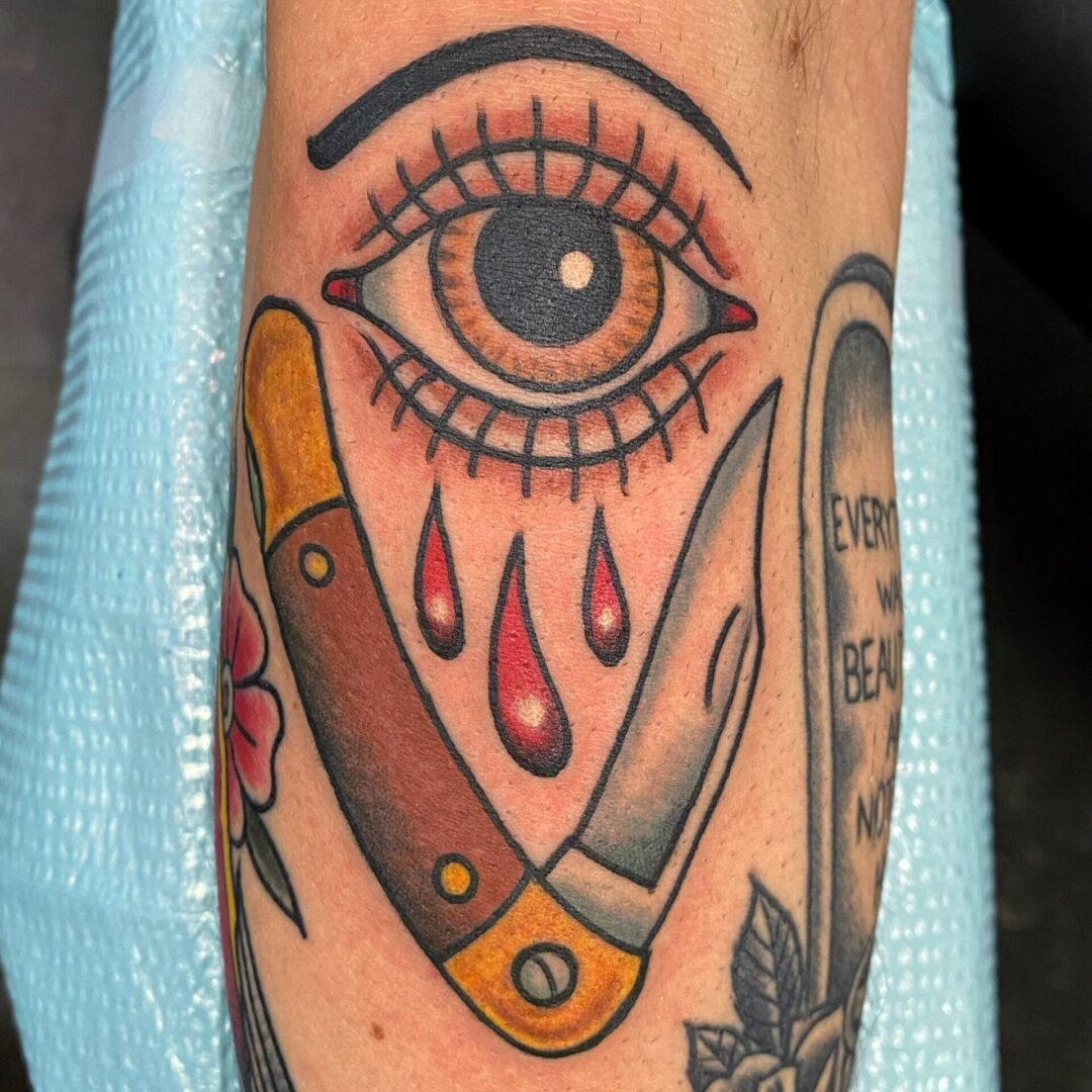 A tattoo of an eye, knife and scissors.