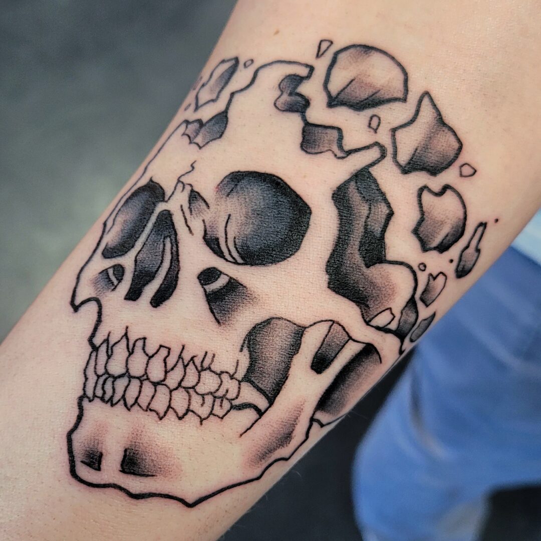 A black and white skull tattoo on the arm of someone.