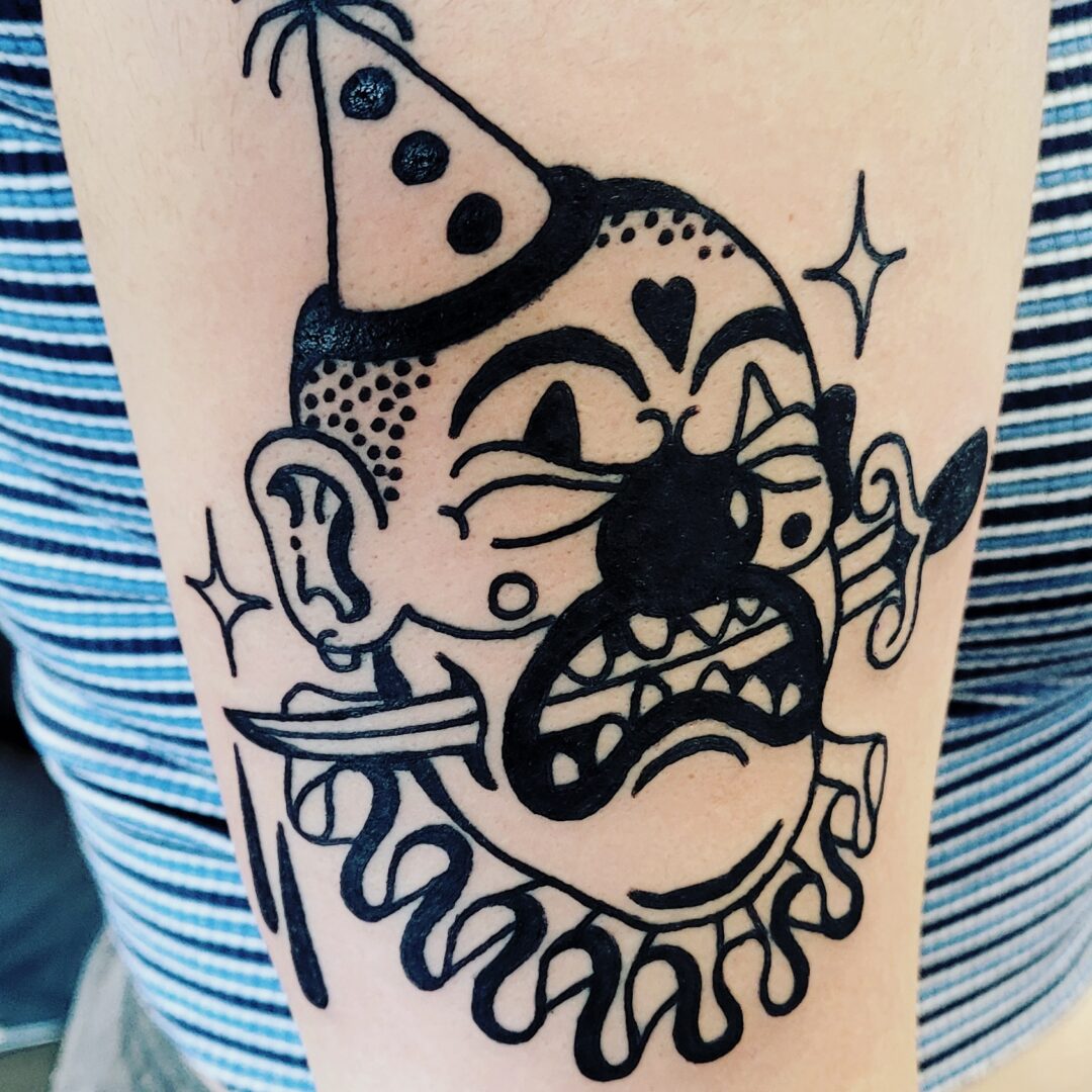 A black and white clown tattoo on the arm of someone.