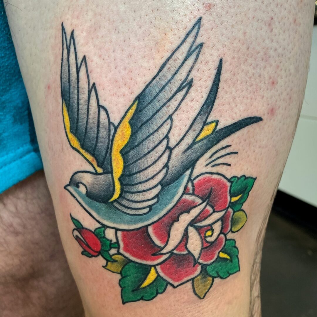 A bird flying over a flower tattoo on the arm.