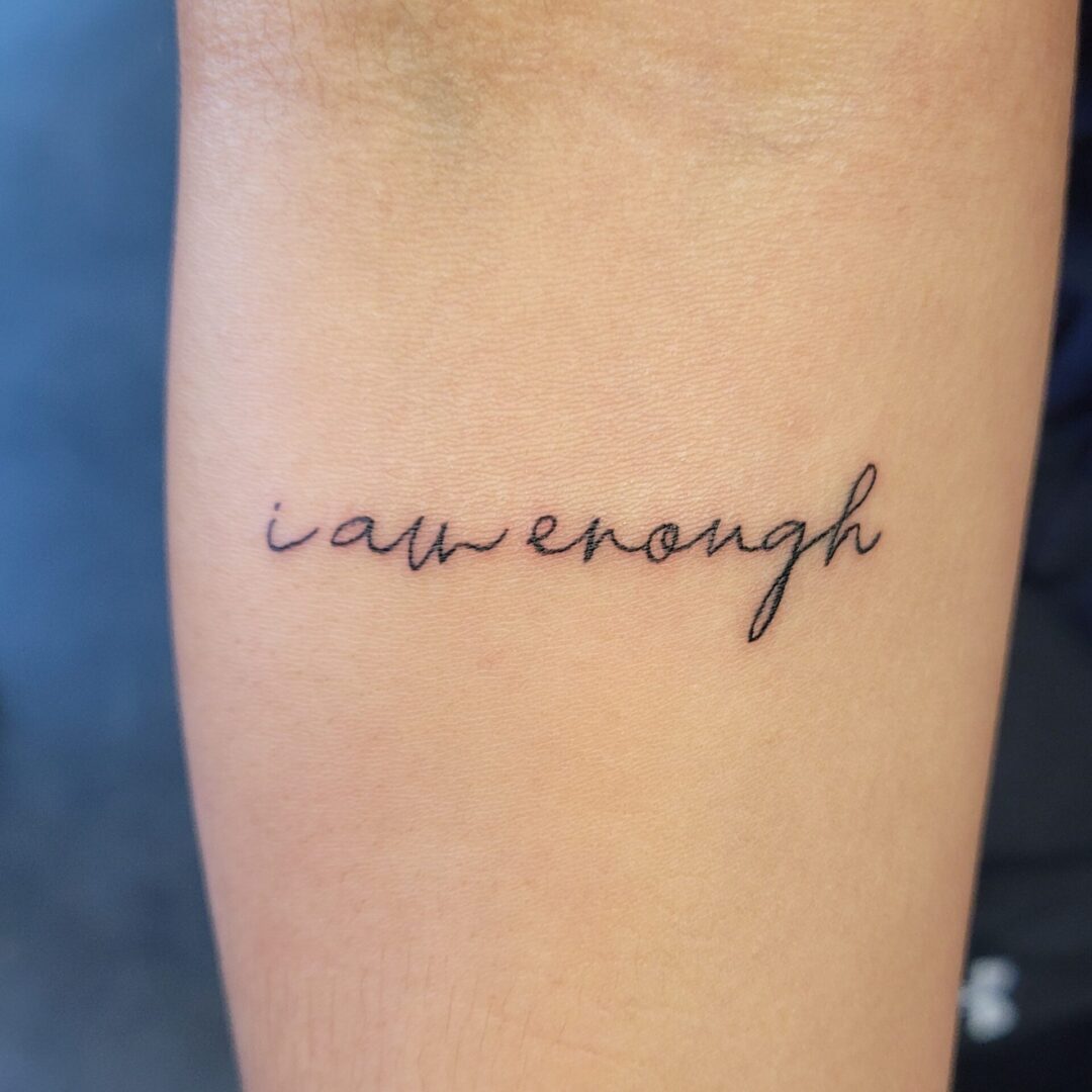 A tattoo that says law enough on the side of a wrist.